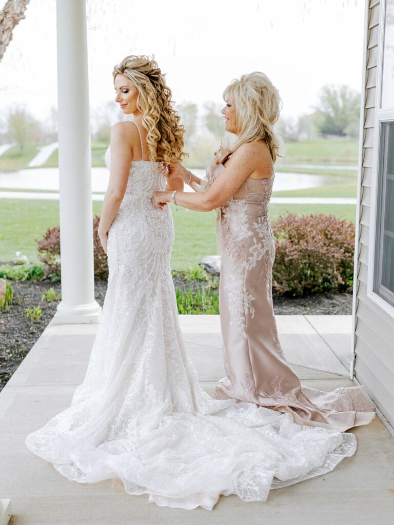 Mother of the bride helping bride into wedding dress