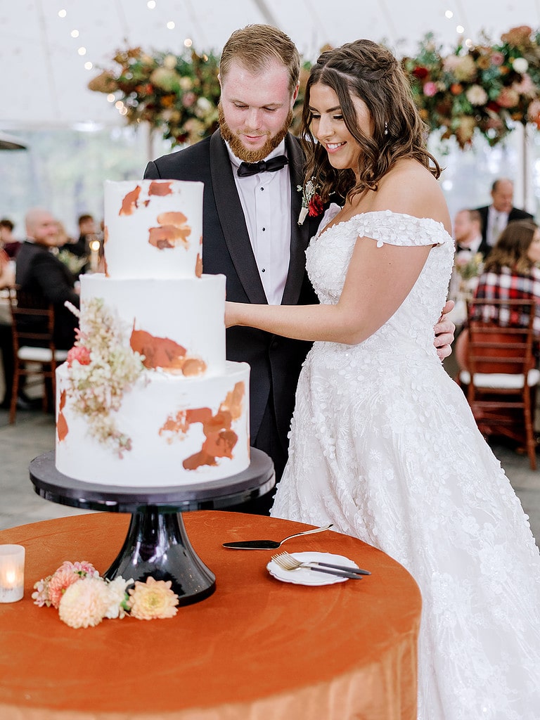 Photo of bride and groom cutting their cake at an outdoor tented fall wedding.