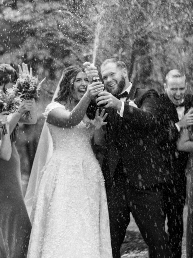 Photo of bride and groom popping champagne with bridesmaids and groomsmen at a fall wedding.