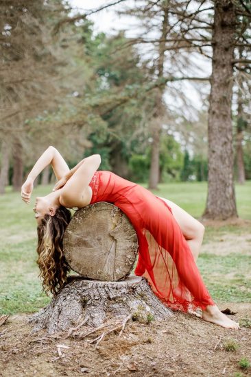 woman laying over cut tree stump wearing red lingerie