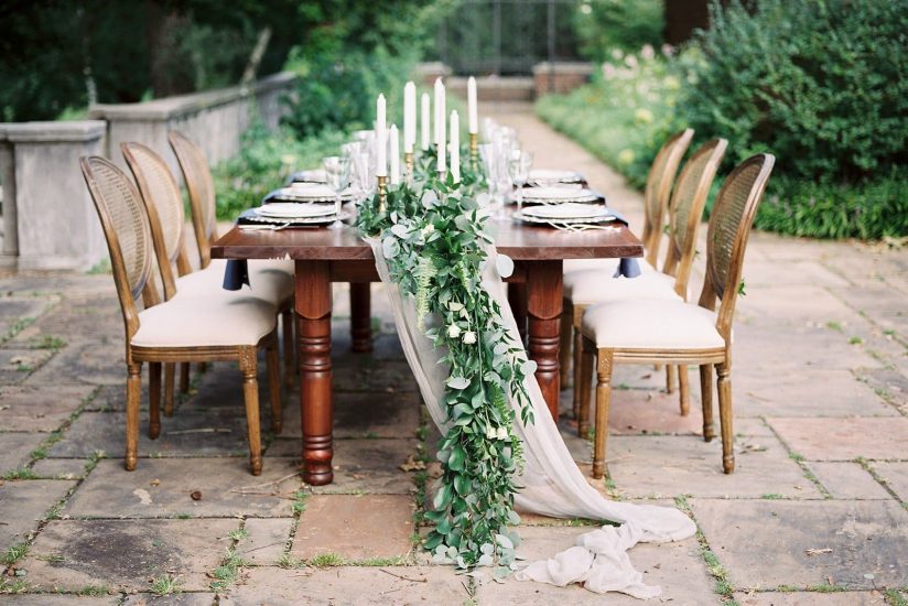English garden table set up with cane back chairs and silk and willow table runner and greenery