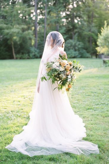 Bridal portrait with veil and bouquet at sunset in the grass