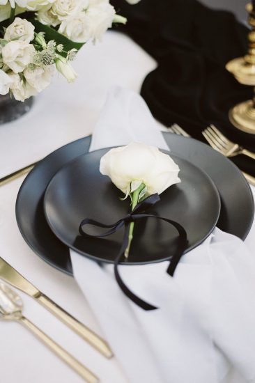 close up details of black matte plates with a rose on top and gold silverware