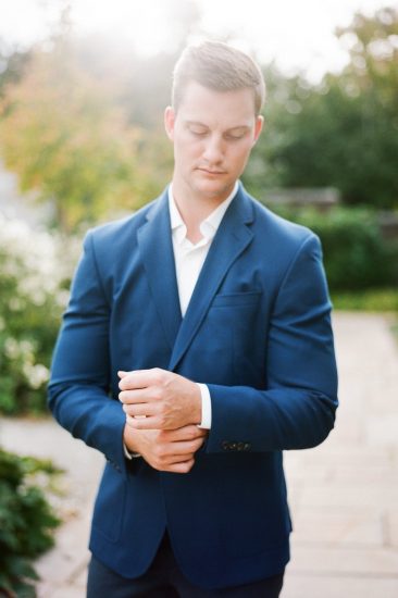 man posing fixing his cufflinks in a blue suit