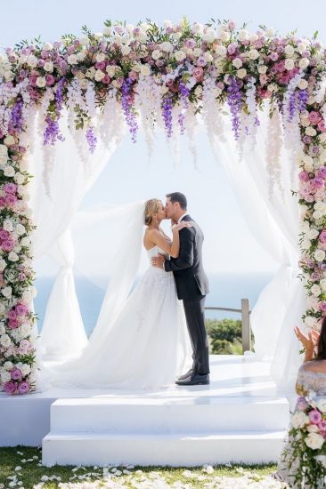 Bride and groom kissing at their ceremony under a chuppah covered with pink and white flowers