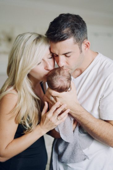 Parents holding and kissing their newborn daughter at home