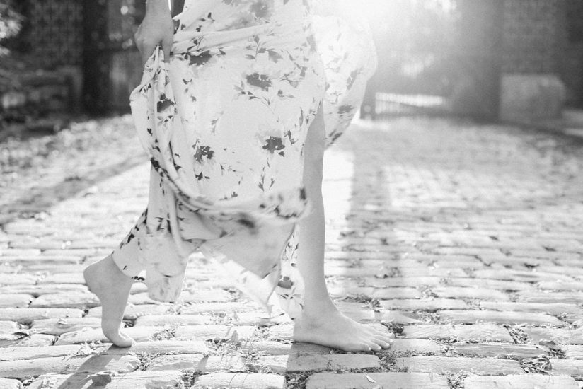 black and white photo of woman walking on cobblestones